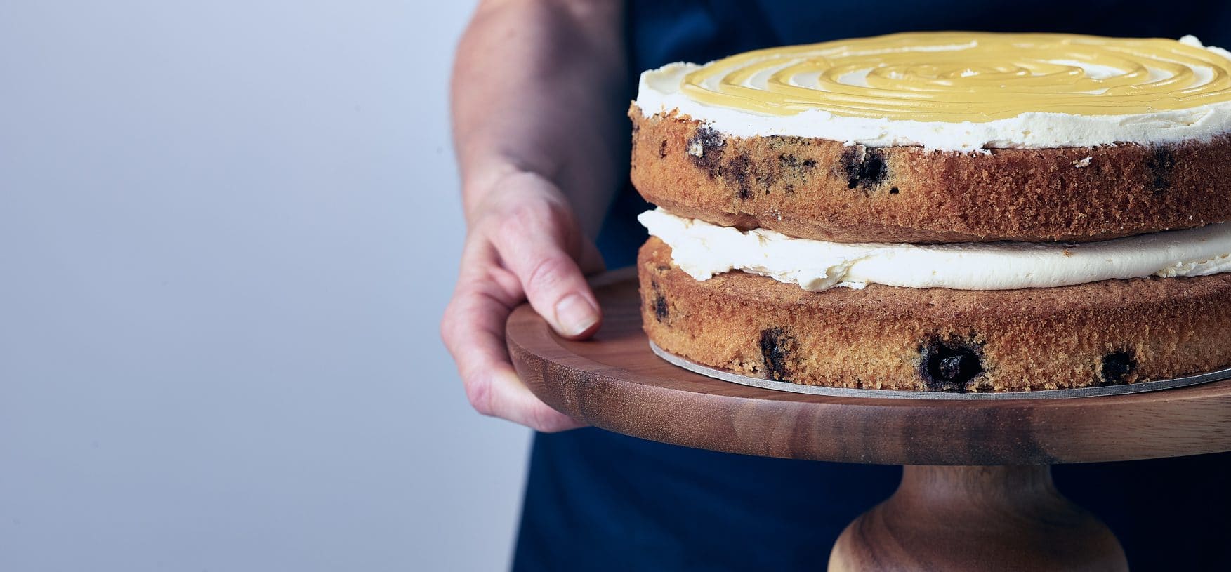 Baker holding double layer lemon and blueberry cake